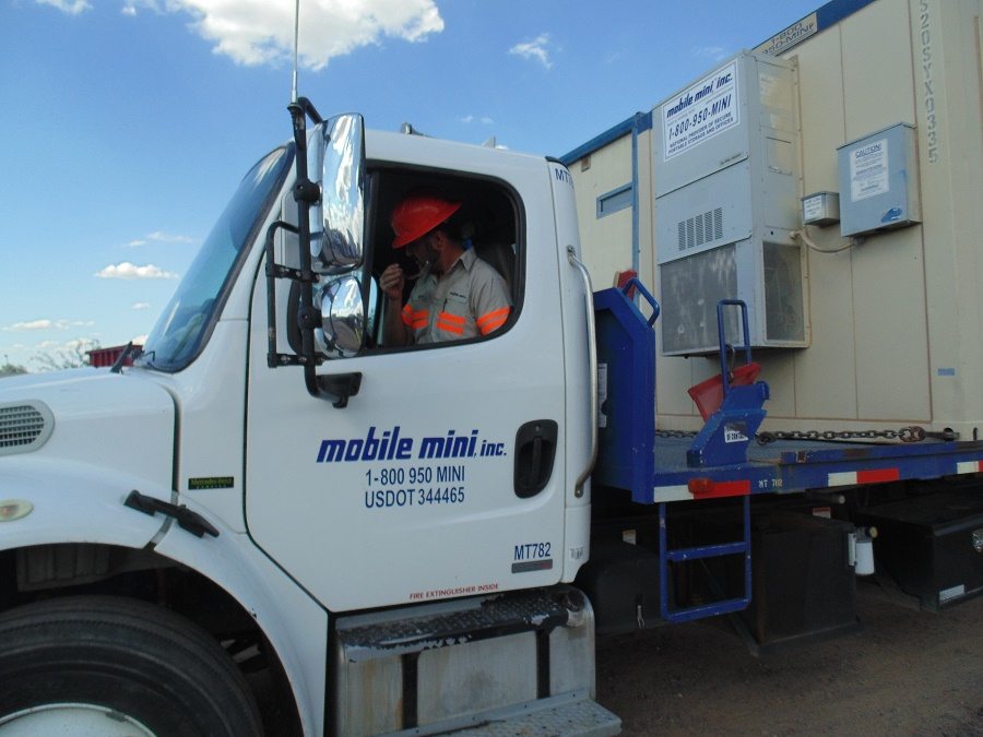 Mobile Mini driver delivering mobile office on flatbed truck and trailer